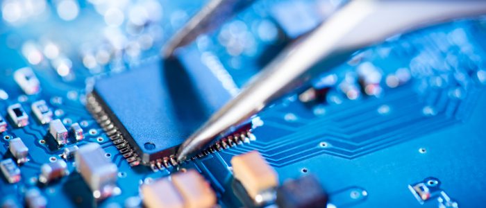 Close-up of a microchip being placed on a blue circuit board.