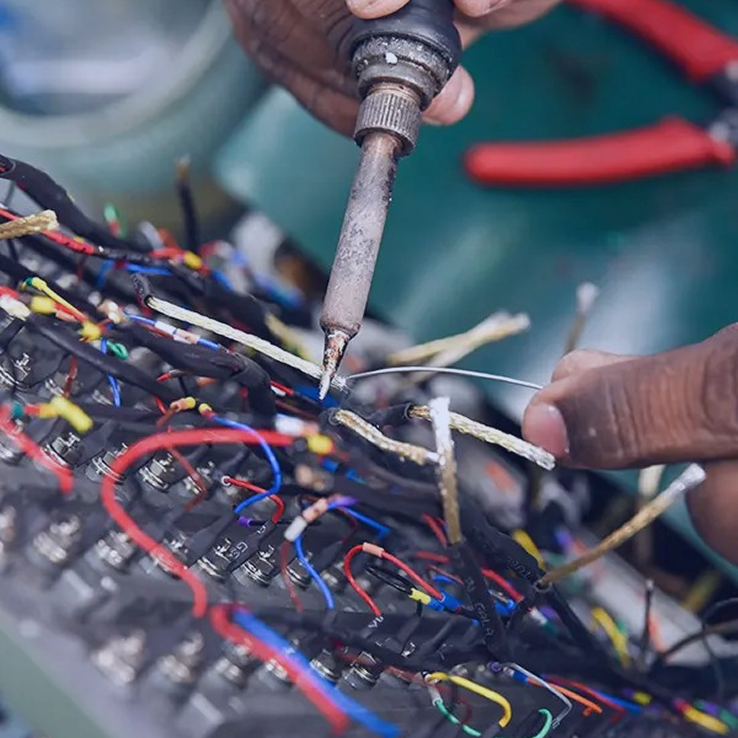 Technician soldering wires on electronic control board during industrial electrical assembly