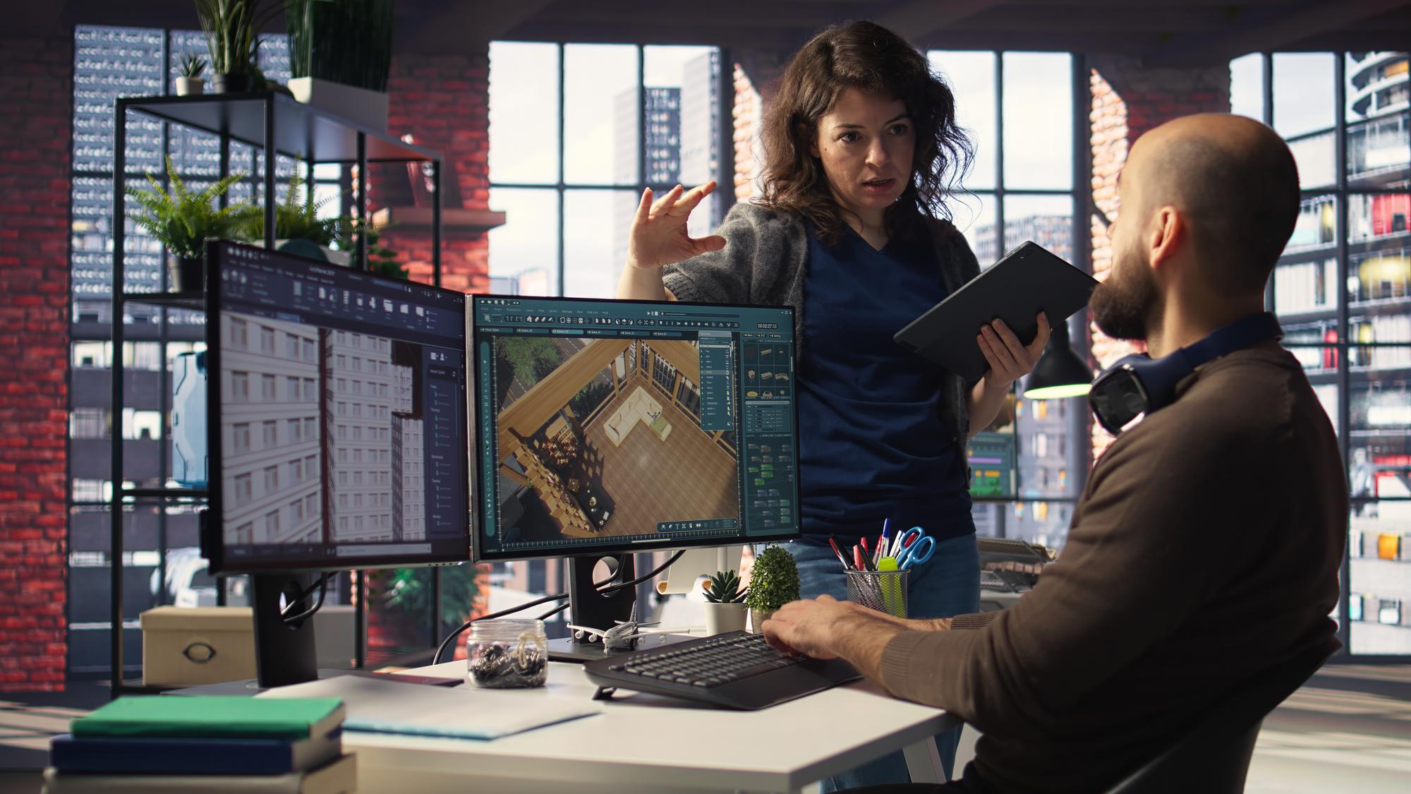 Architects collaborating in office using dual monitors to design 3D building interior model