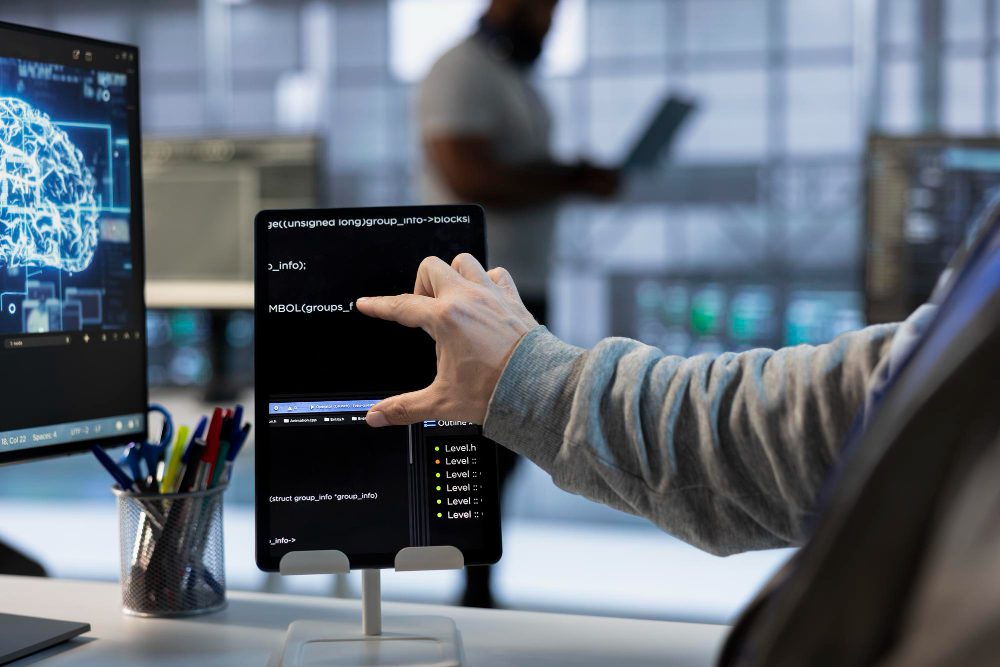 Developer interacting with tablet showing AI code and neural network interface in a modern tech office