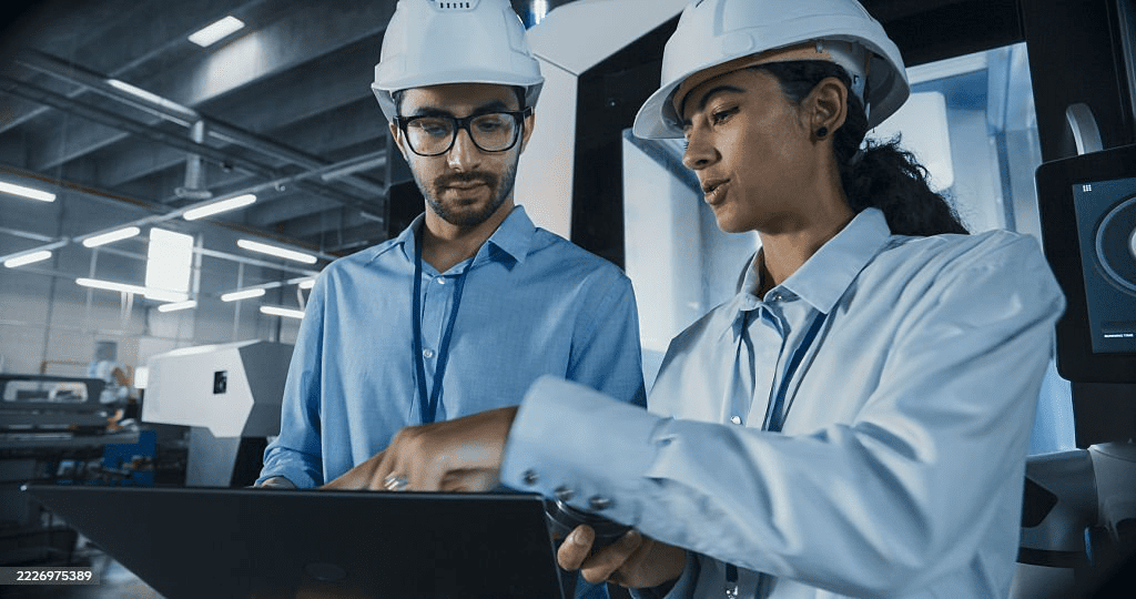 Engineers in safety helmets reviewing production data on a tablet inside an industrial manufacturing facility