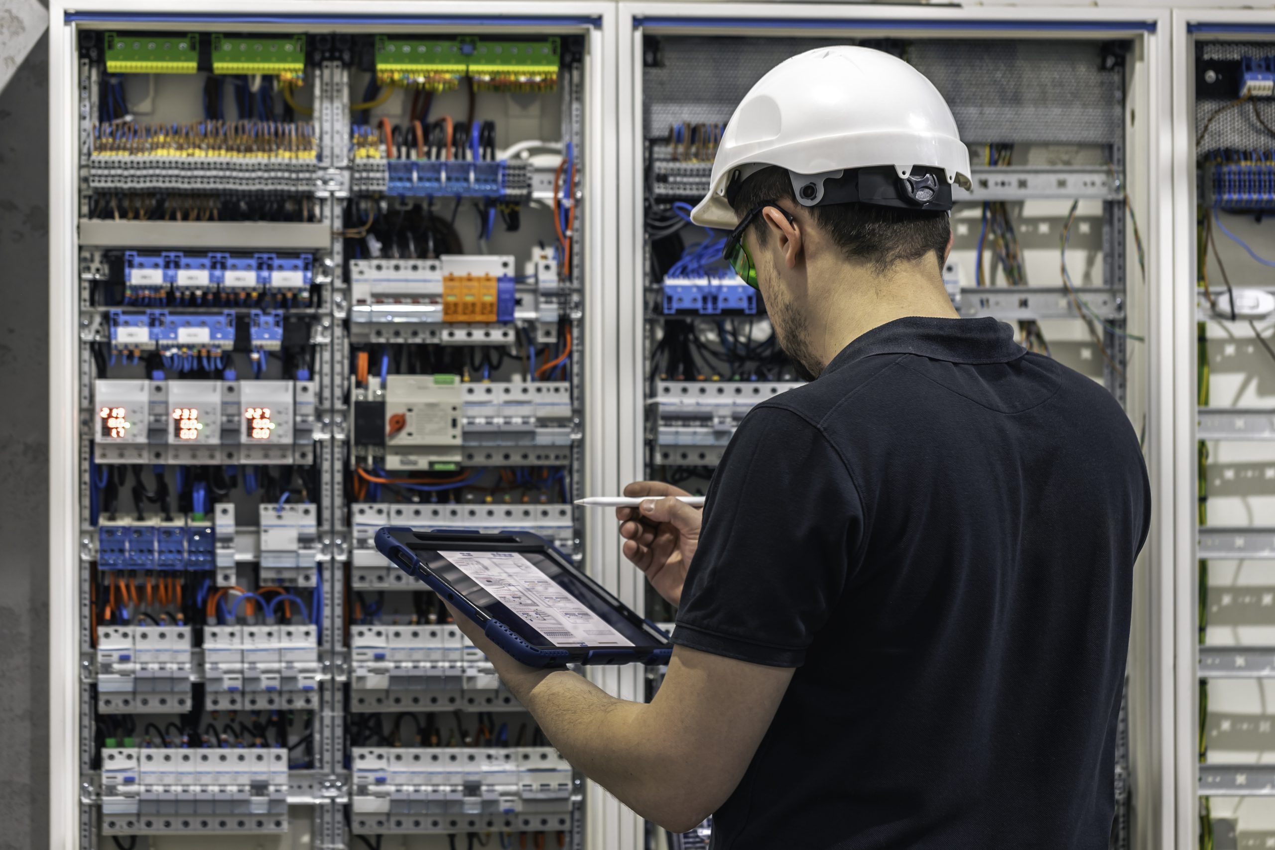 Technician inspecting electrical control panels using tablet for industrial automation and system diagnostics