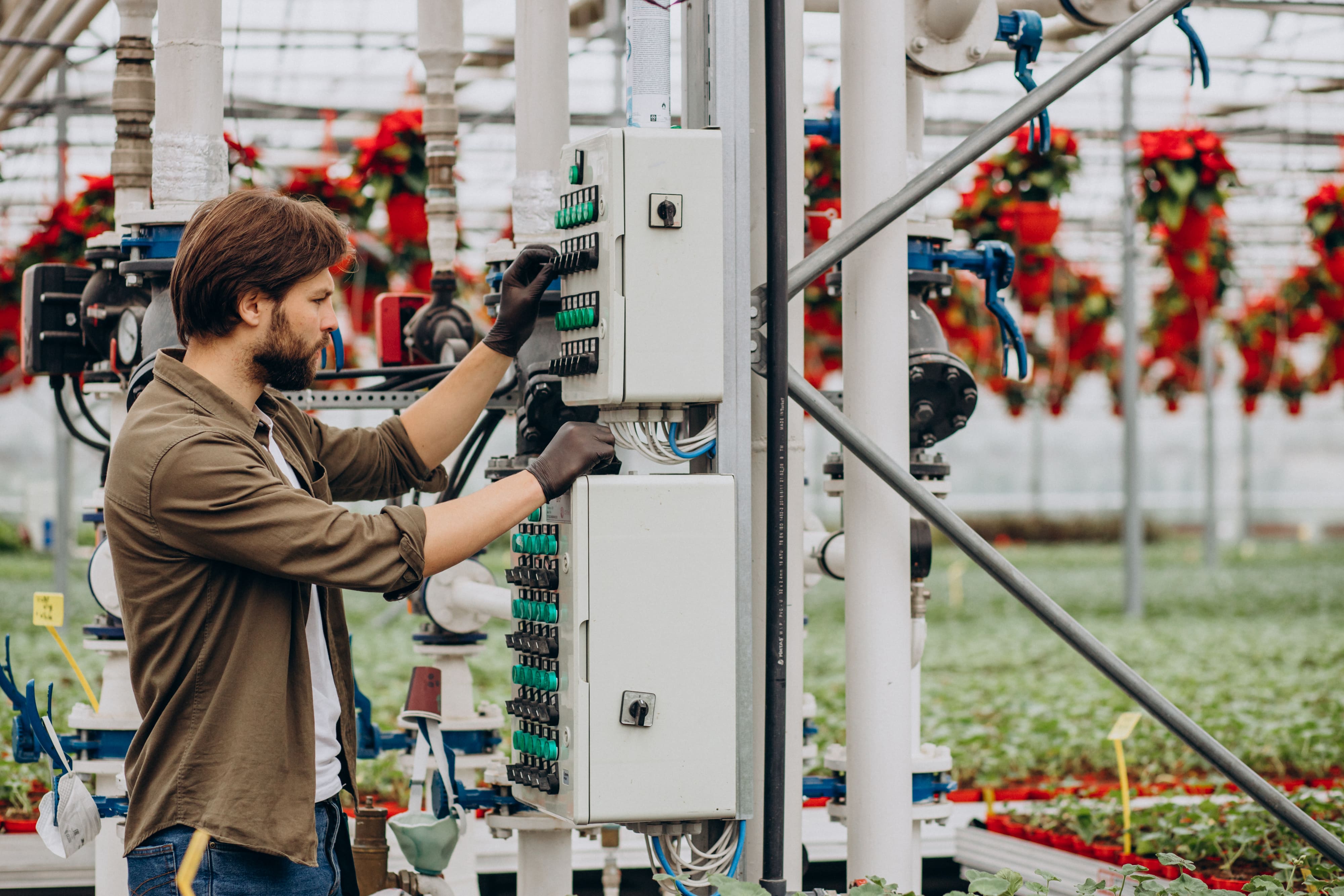 Technician operating an industrial control panel inside a greenhouse automation system