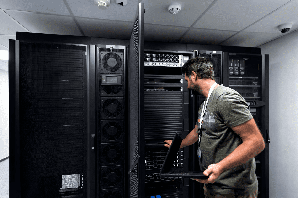 Data center technician inspecting server rack while using laptop for system maintenance and monitoring